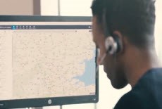 Man wearing headphones looking at a computer monitor with a map showing