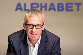 Head shot of Alphabet (GB) CEO Mike Dennett with logo on wall in background