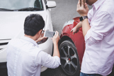 Man taking a picture of a crashed car while standing next to someone on the phone