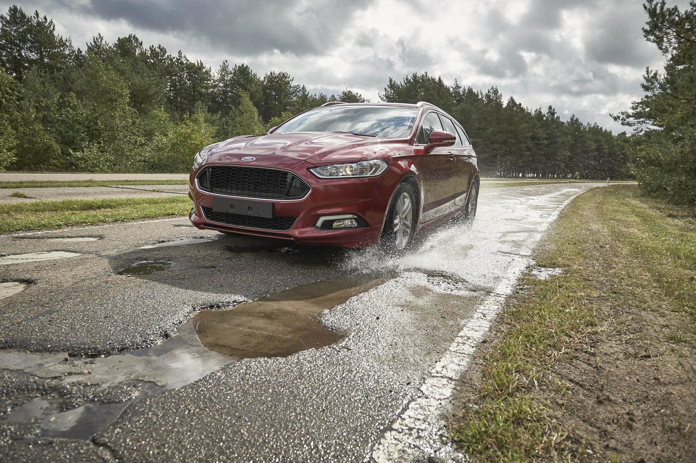 Car driving along a stretch of road covered in potholes