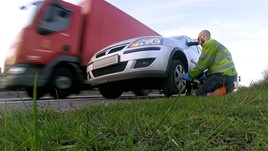 Roadside recovery worker changing the wheel on a car by the side of a busy road