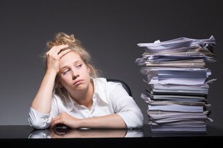 Woman with head in hand sat at desk next to pile of paperwork